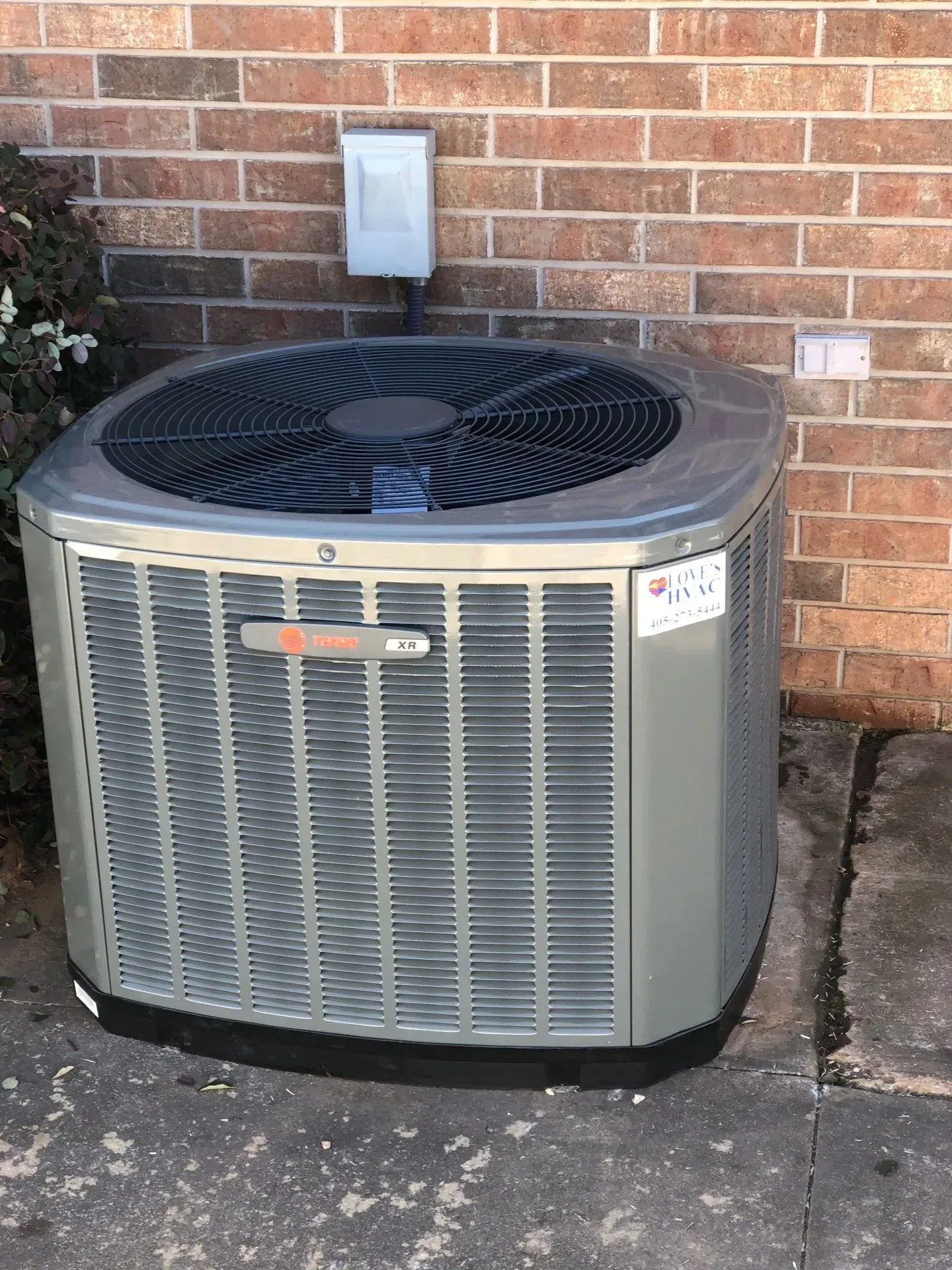 Outdoor air conditioning unit beside a brick wall and concrete path