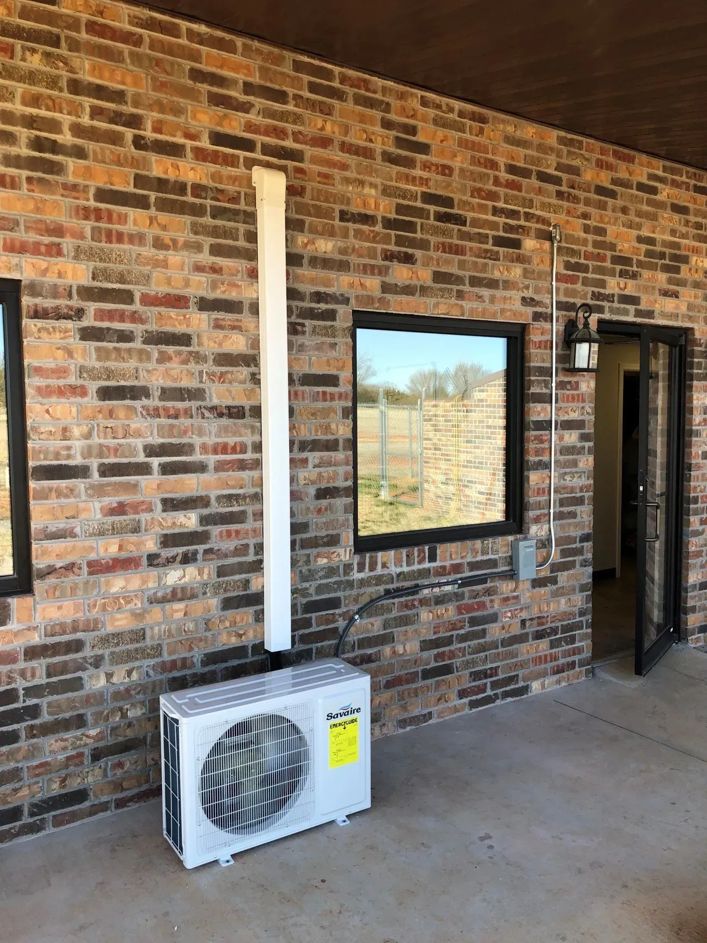 Brick exterior wall with windows and a wall-mounted air conditioner unit under a covered walkway