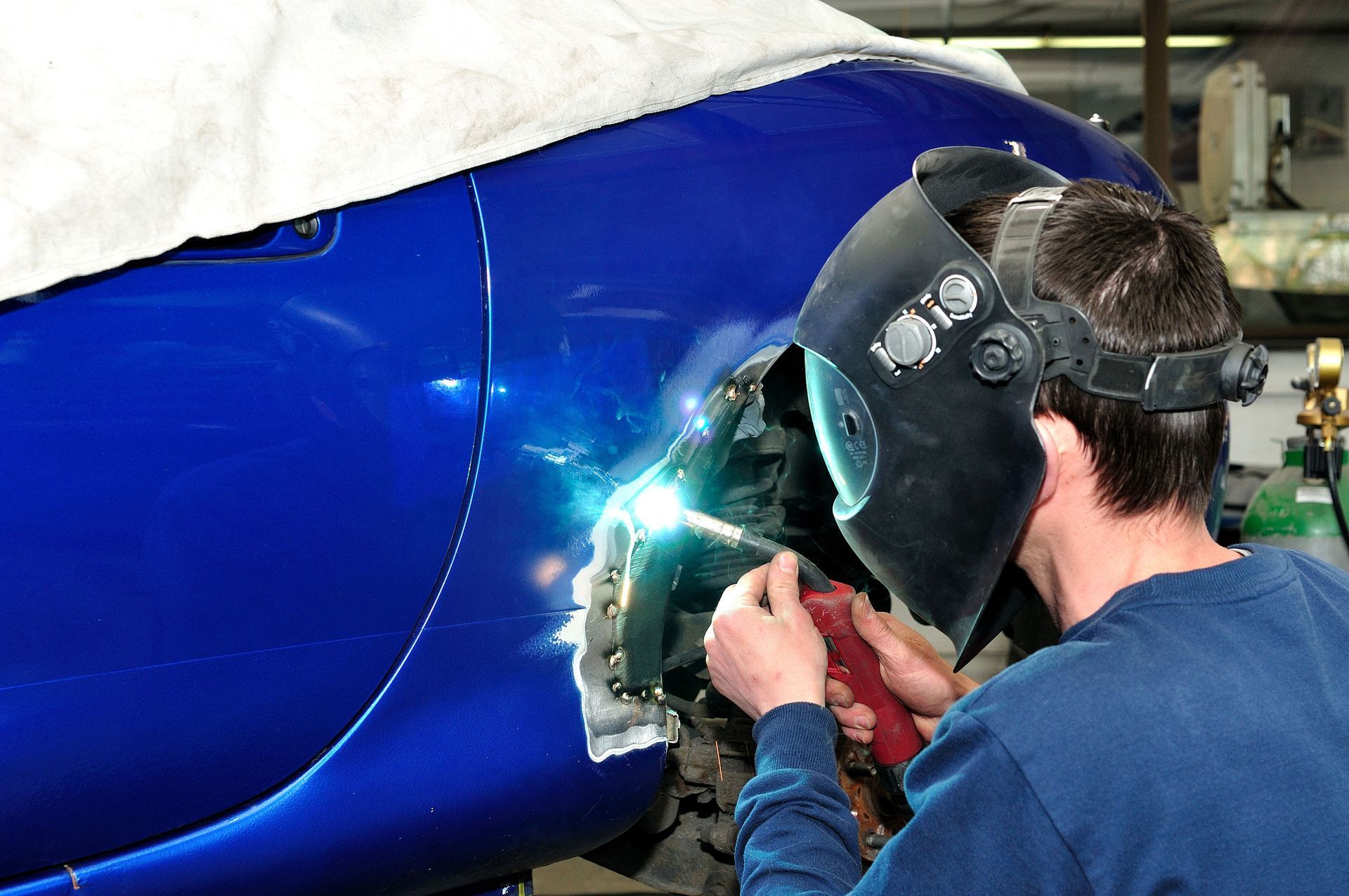 Worker welding blue metal panel while wearing a protective face shield