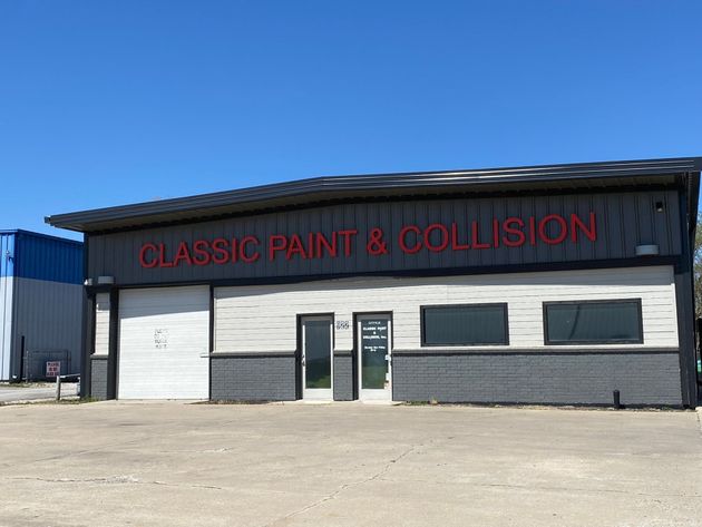 Classic Paint & Collision auto body shop with dark exterior, white garage door, and red sign under a blue sky