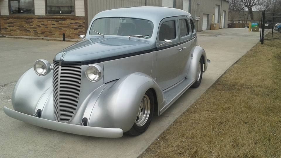Vintage silver custom sedan parked in a driveway outside a building