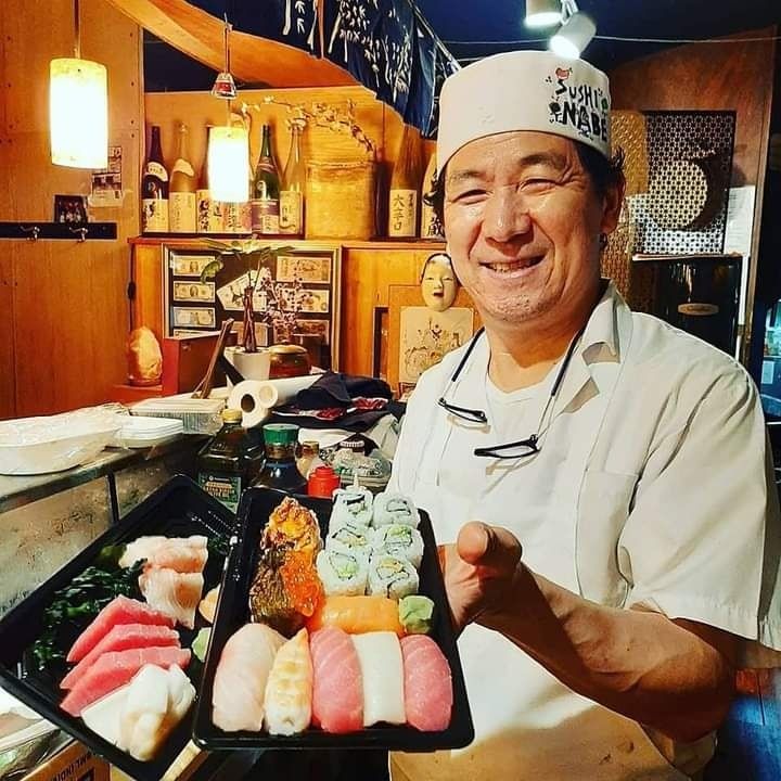 A man in a chef 's hat is holding a tray of sushi