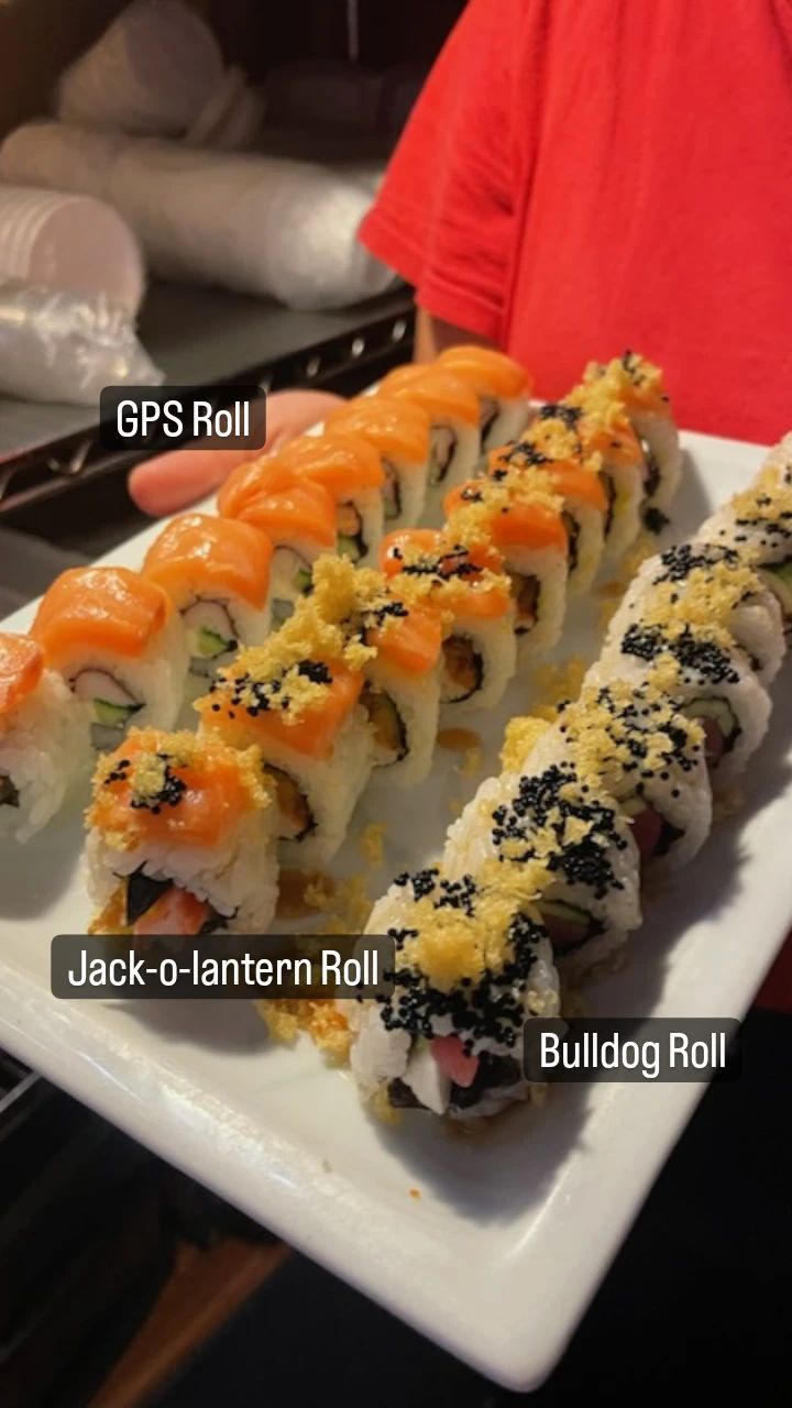 A person is holding a plate of sushi including jack-a-lantern roll and bulldog roll