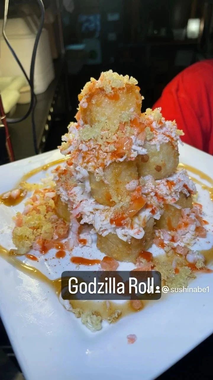 A white plate topped with a stack of food called godzilla roll