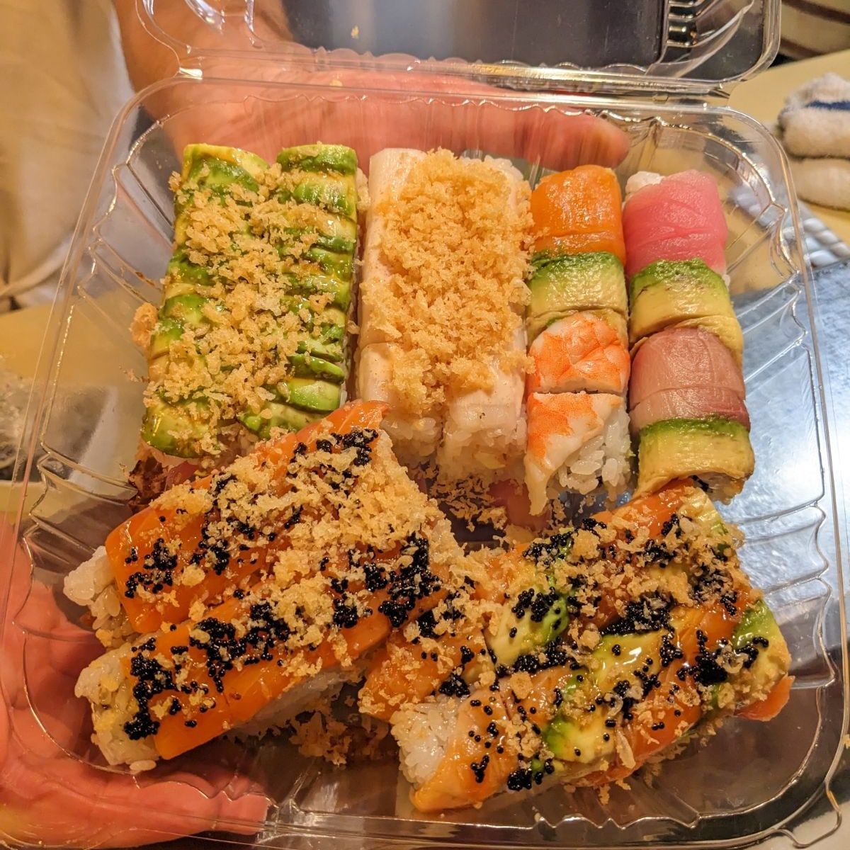 A person is holding a plastic container filled with sushi rolls.