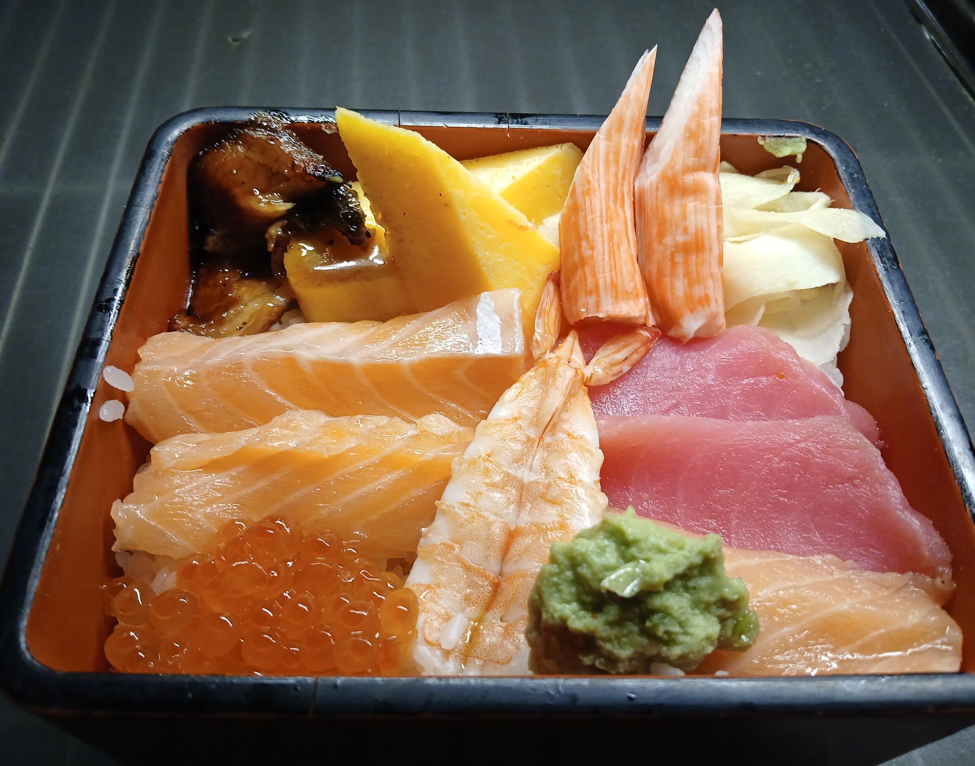 A square bowl filled with different types of food including salmon and shrimp