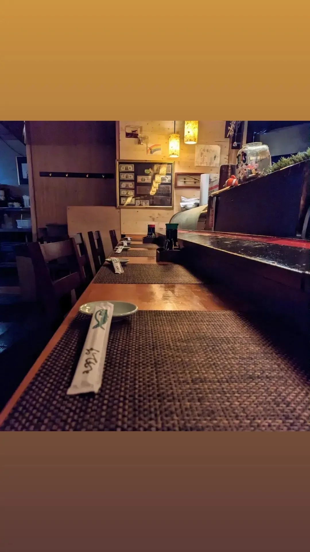 A long table in a restaurant with plates and chopsticks on it.