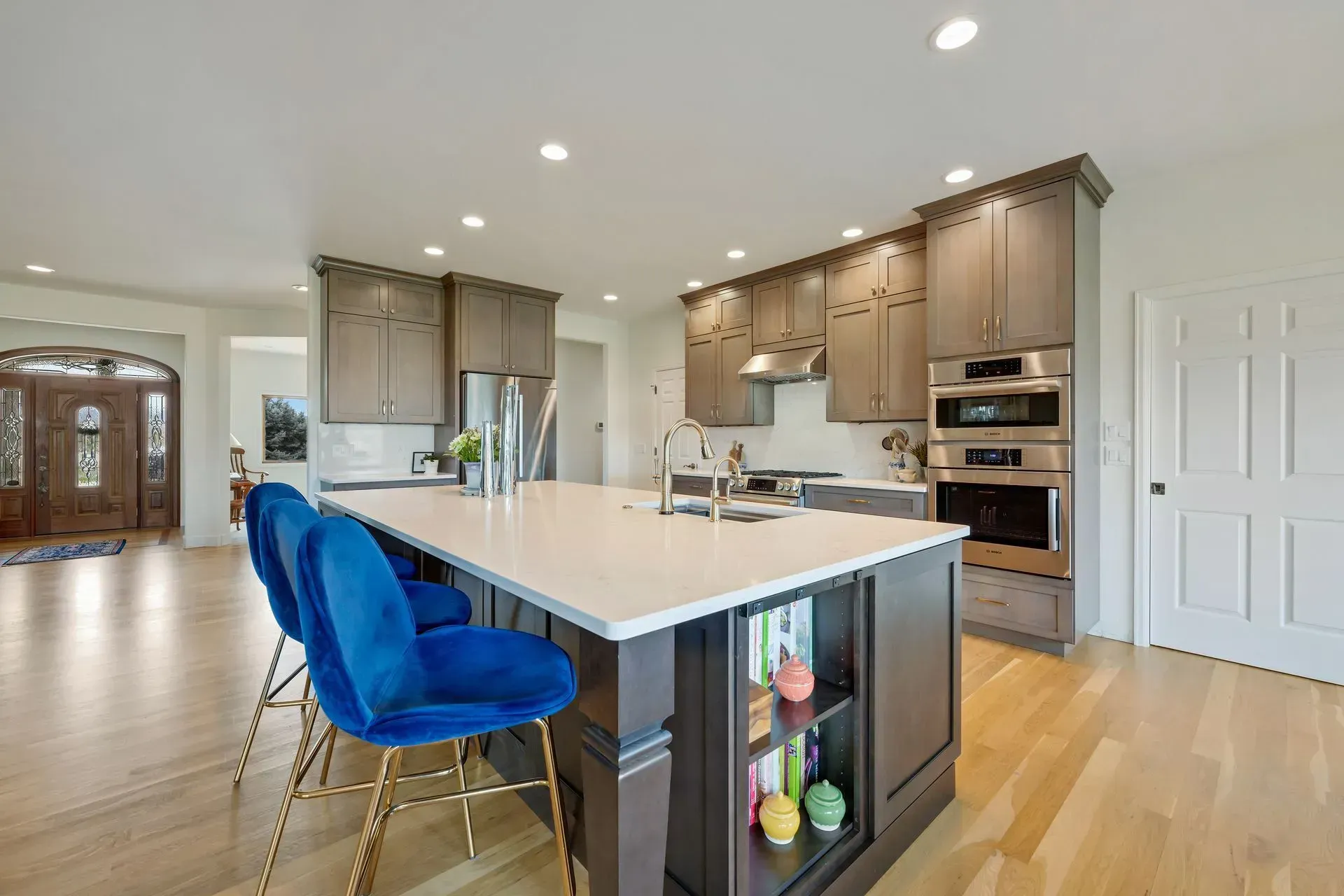 Spacious kitchen with a large island, blue velvet bar stools, and light wood floors.