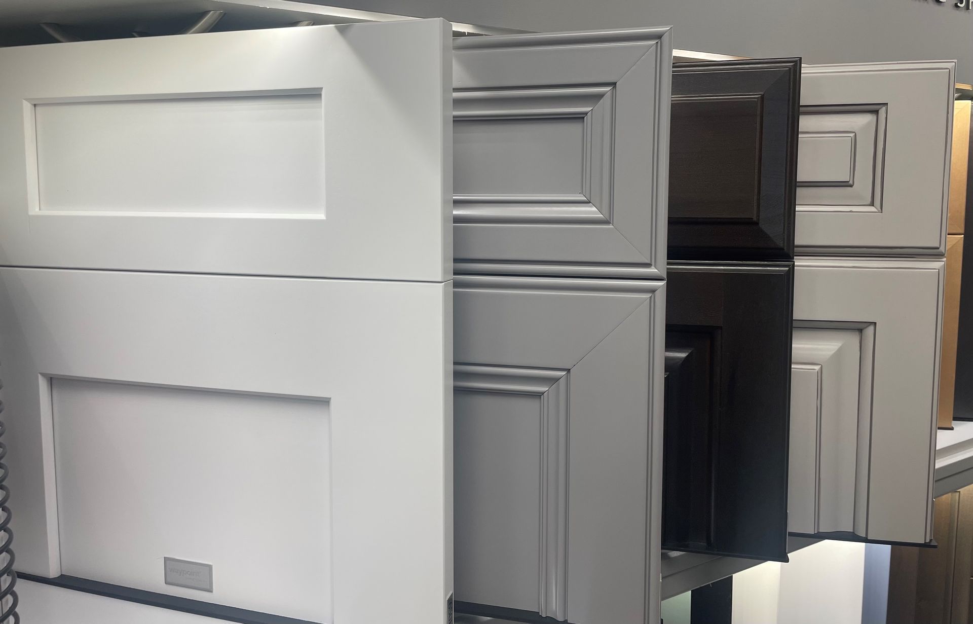 Cabinet door samples in white, gray, and dark brown, stacked on a shelf.
