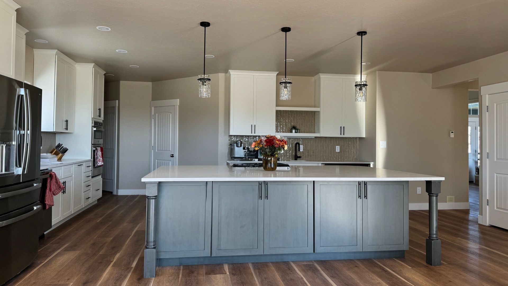 Modern kitchen with gray and white cabinets, large island, pendant lights, and wooden floors.