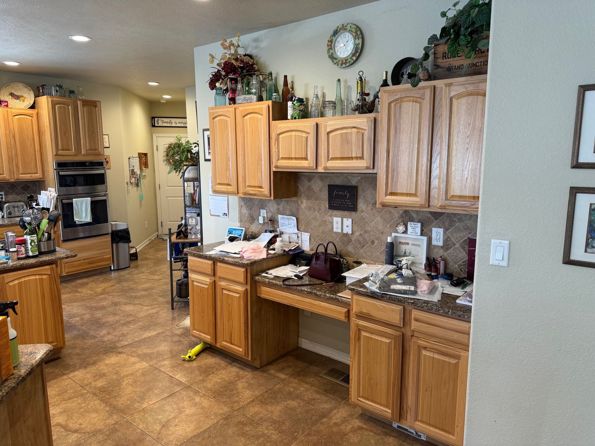 Kitchen with oak cabinets, cluttered counters, and tile flooring.