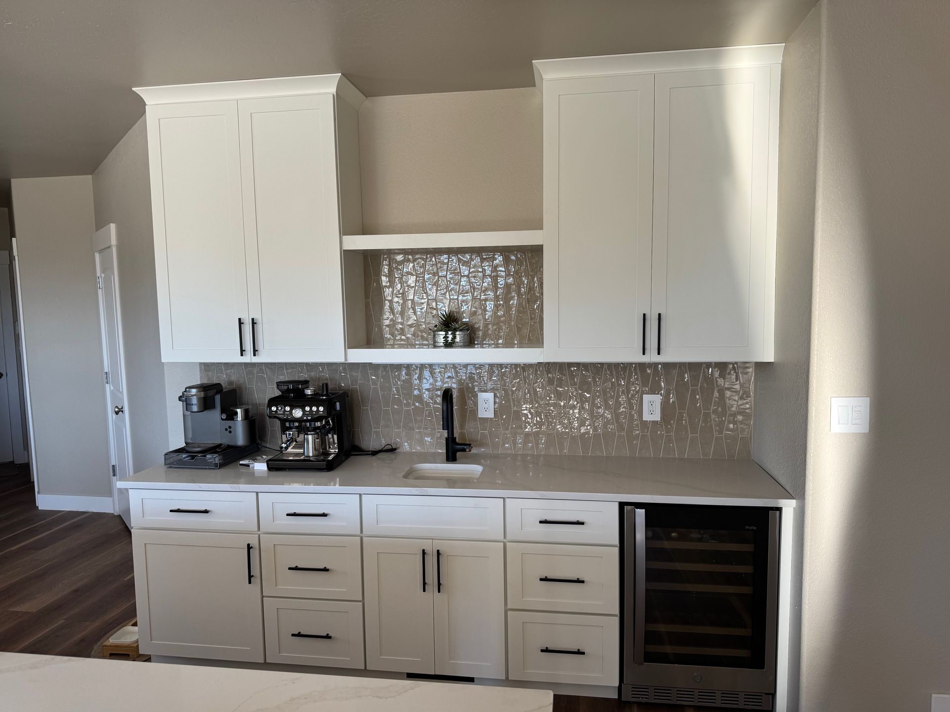 White built-in coffee and wine bar with upper cabinets, countertops, and a wine fridge.