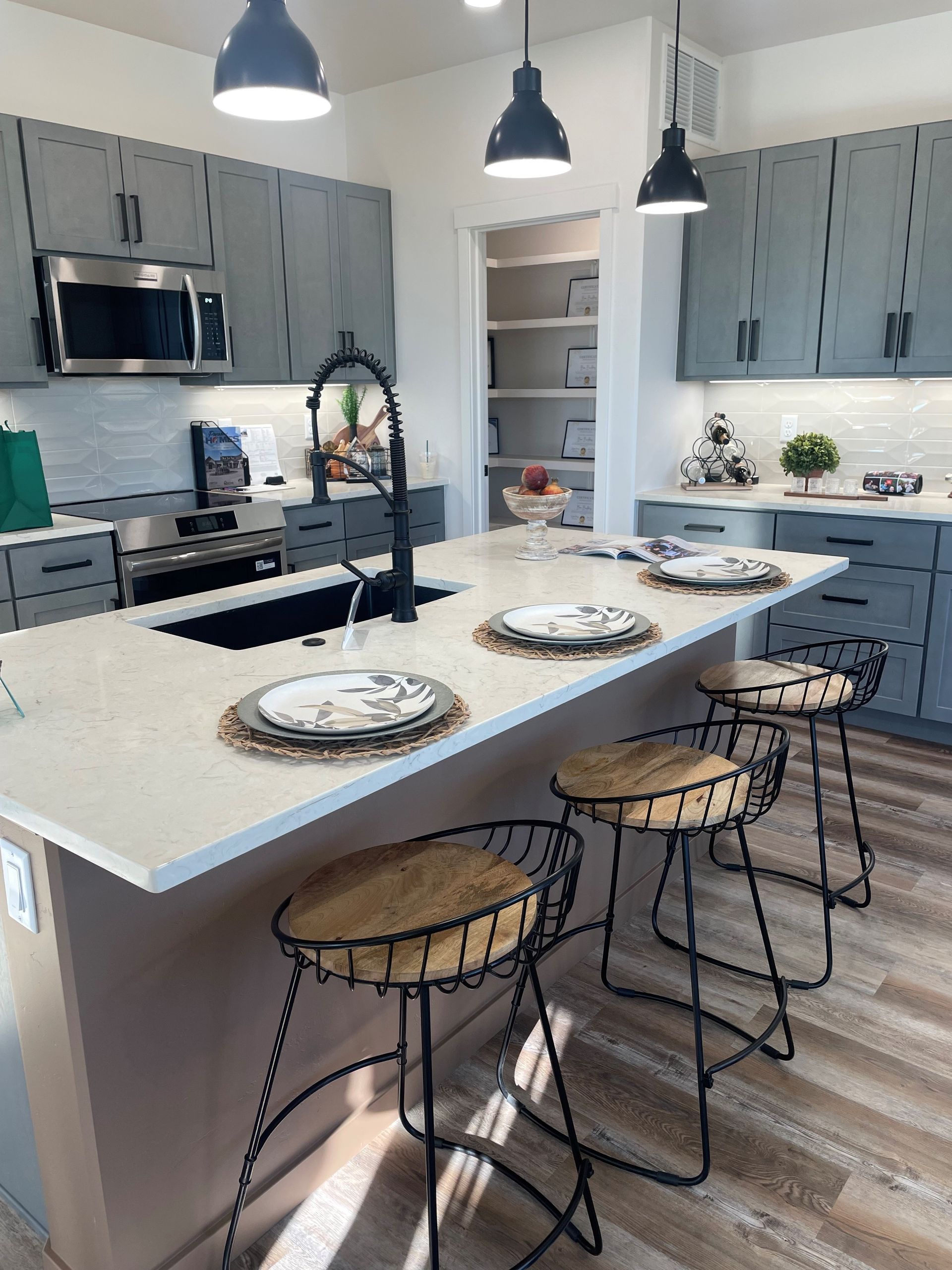 Modern kitchen with island, gray cabinets, stainless steel appliances, and black pendant lights.