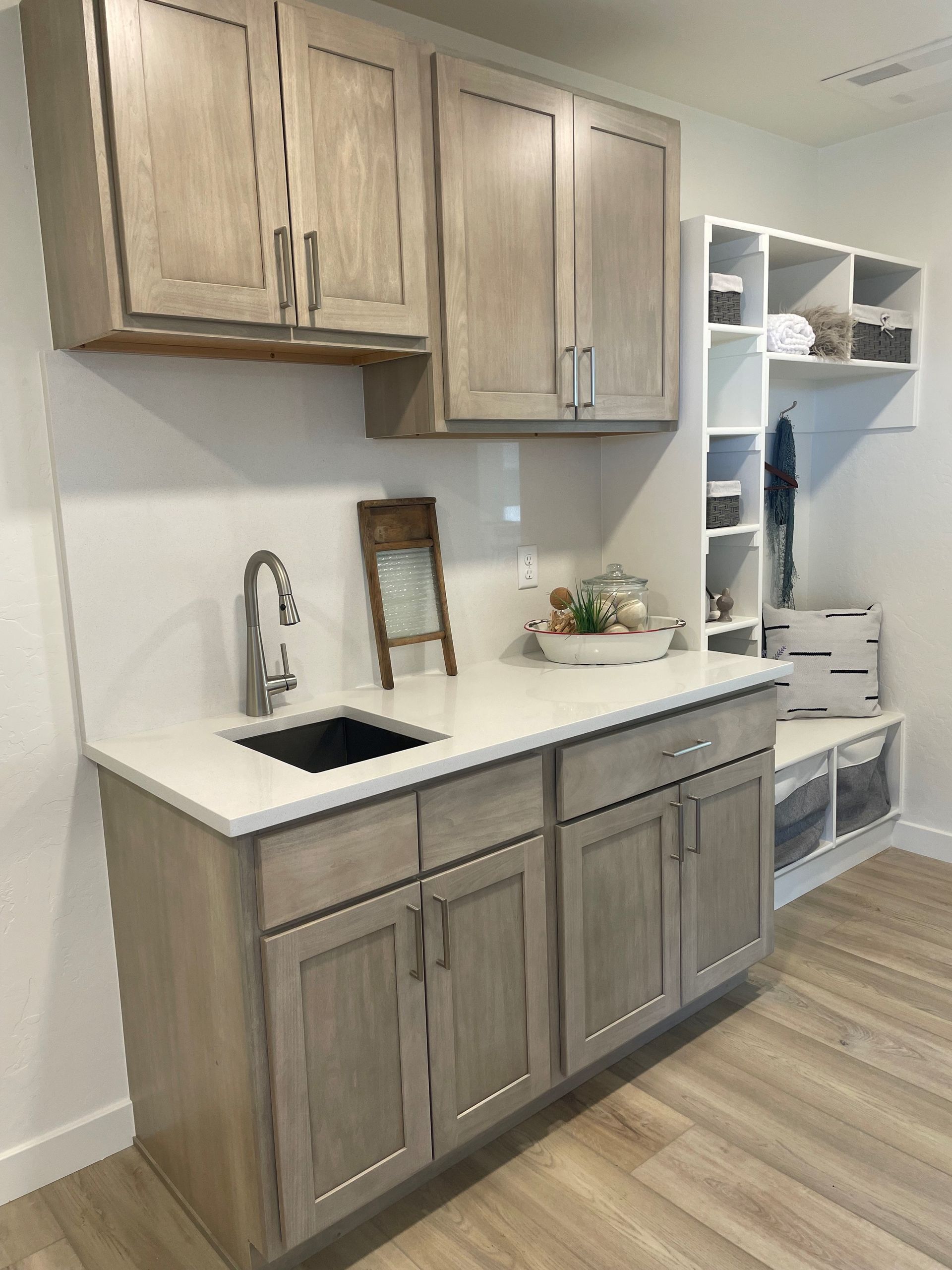 Laundry room with light wood cabinets, white countertop, sink, and open shelving.