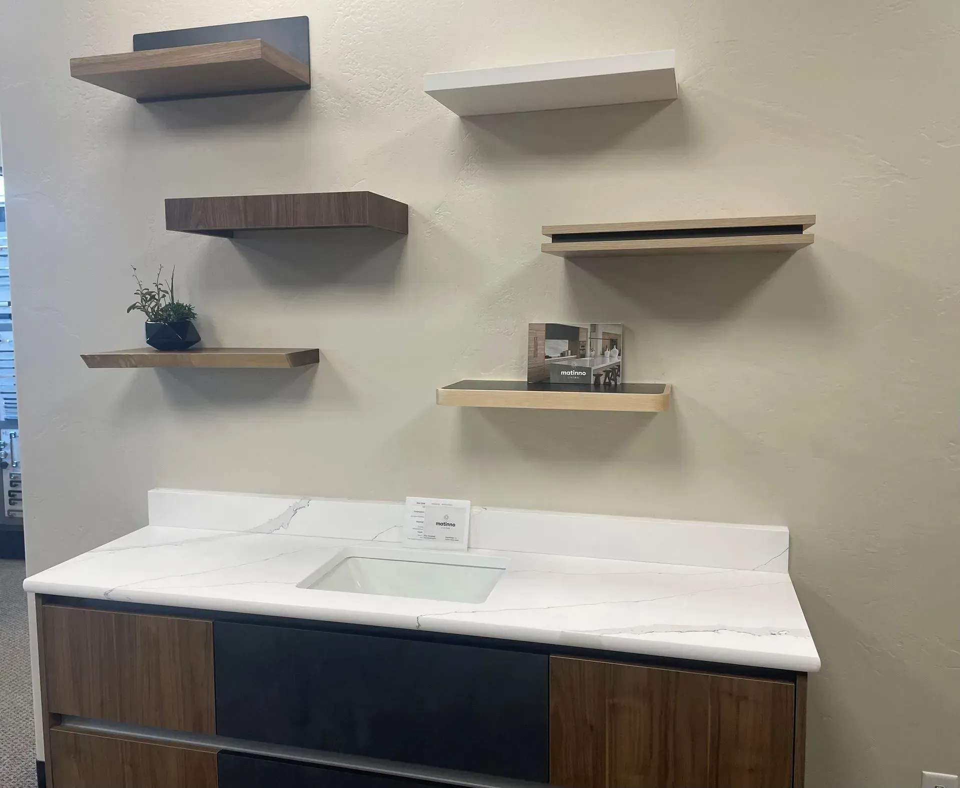 Floating shelves of varying wood tones on a wall above a countertop with a sink.