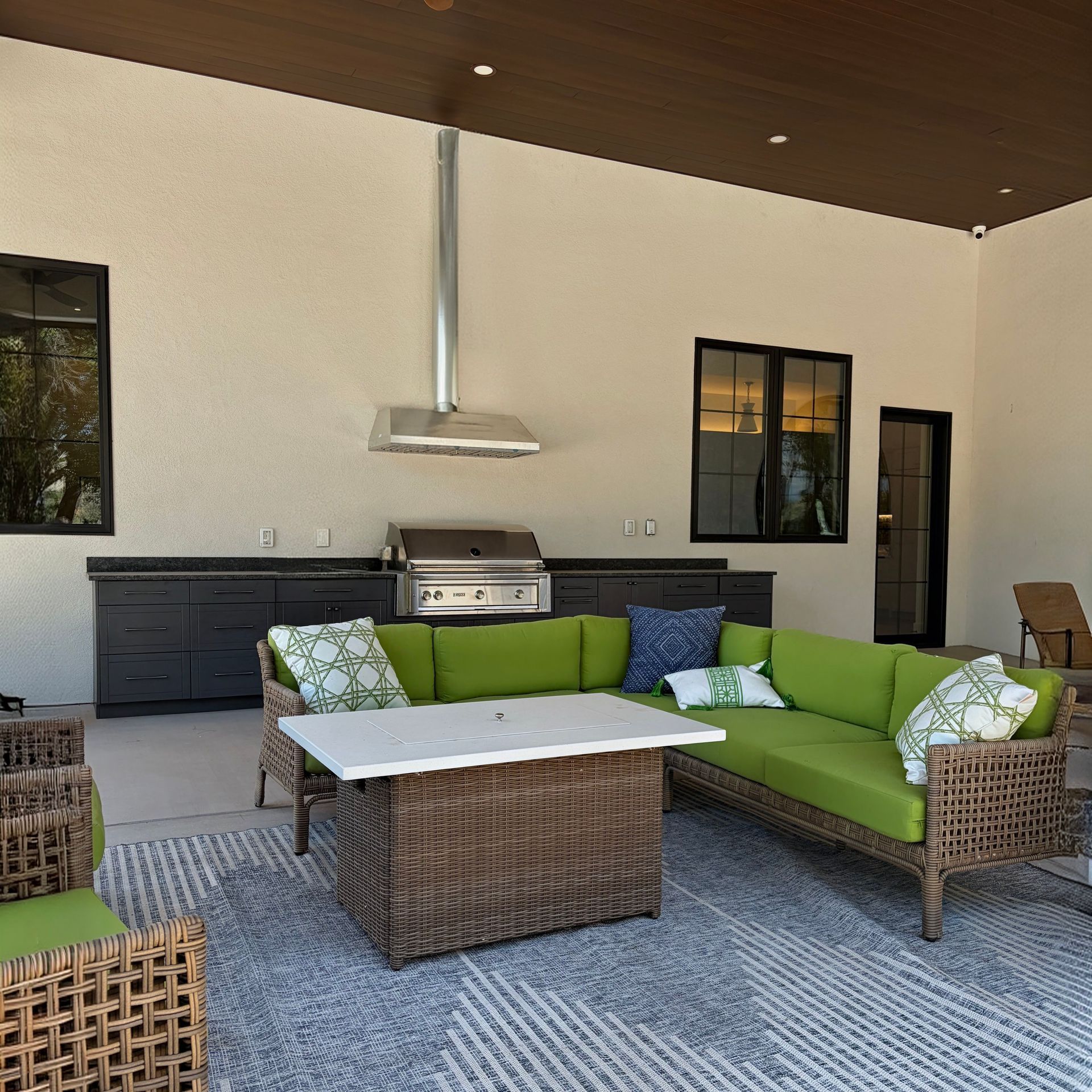 Covered patio with wicker seating, green cushions, and an outdoor kitchen grill area