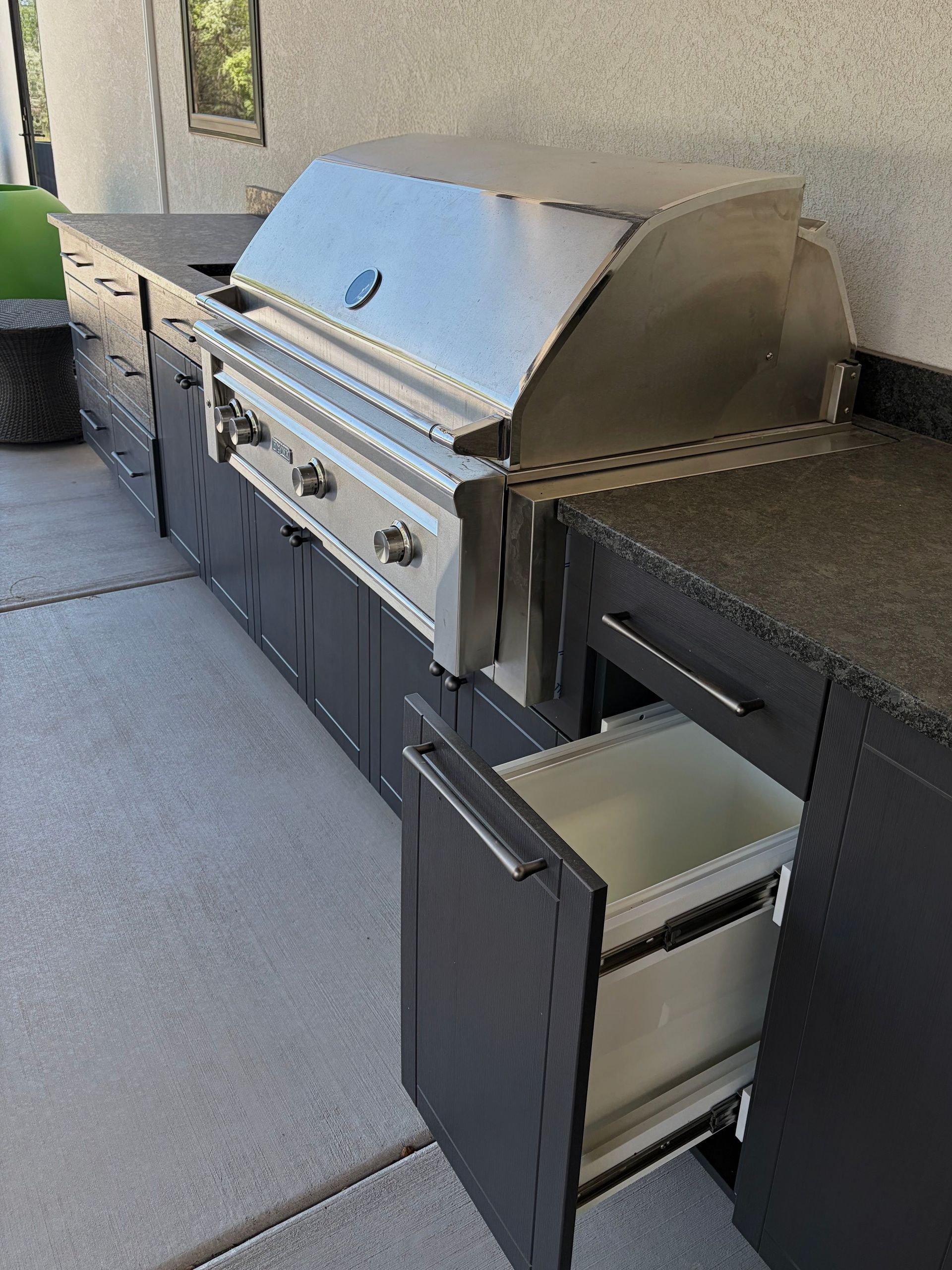 Outdoor patio with a built-in stainless steel grill, countertop, and open storage drawers