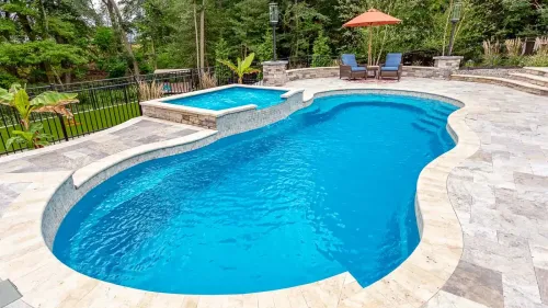 Curved blue swimming pool with stone deck, lounge chairs, and orange umbrella in a tropical backyard