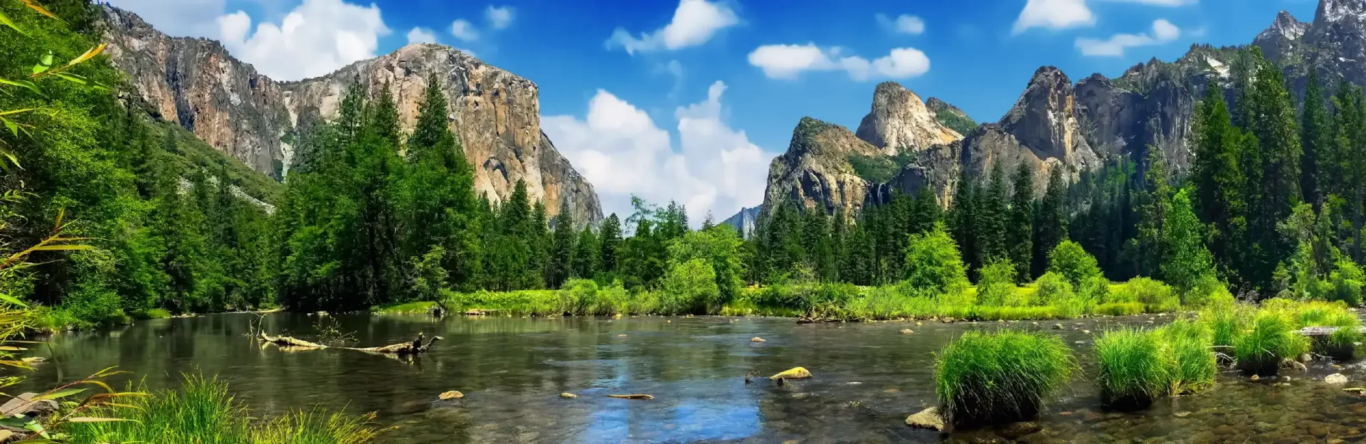 Mountain river landscape with lush green trees, rocky cliffs, and blue sky reflected in calm water