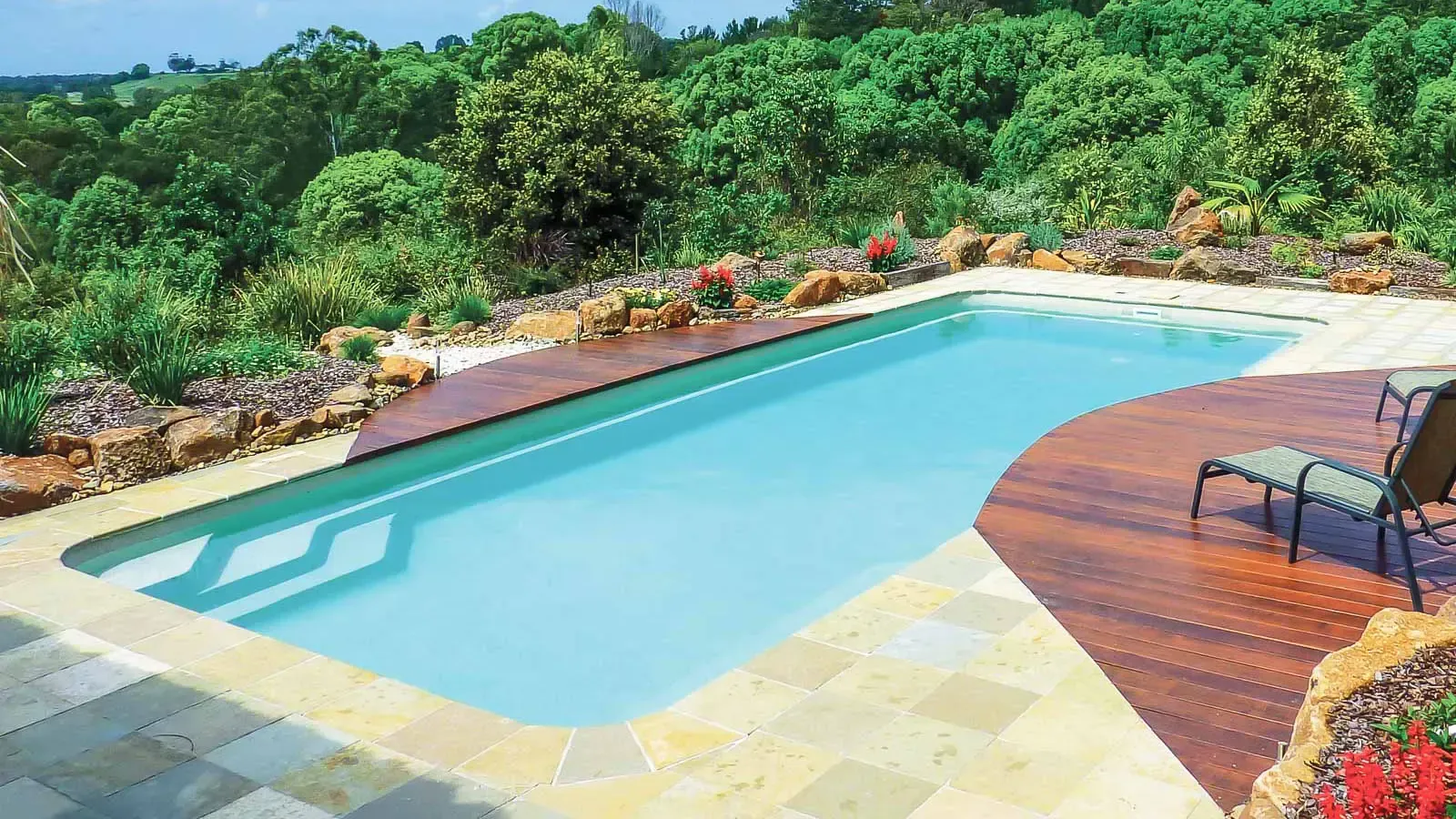 Outdoor swimming pool with clear blue water, tiled deck, lounge chair, and lush green hillside backdrop