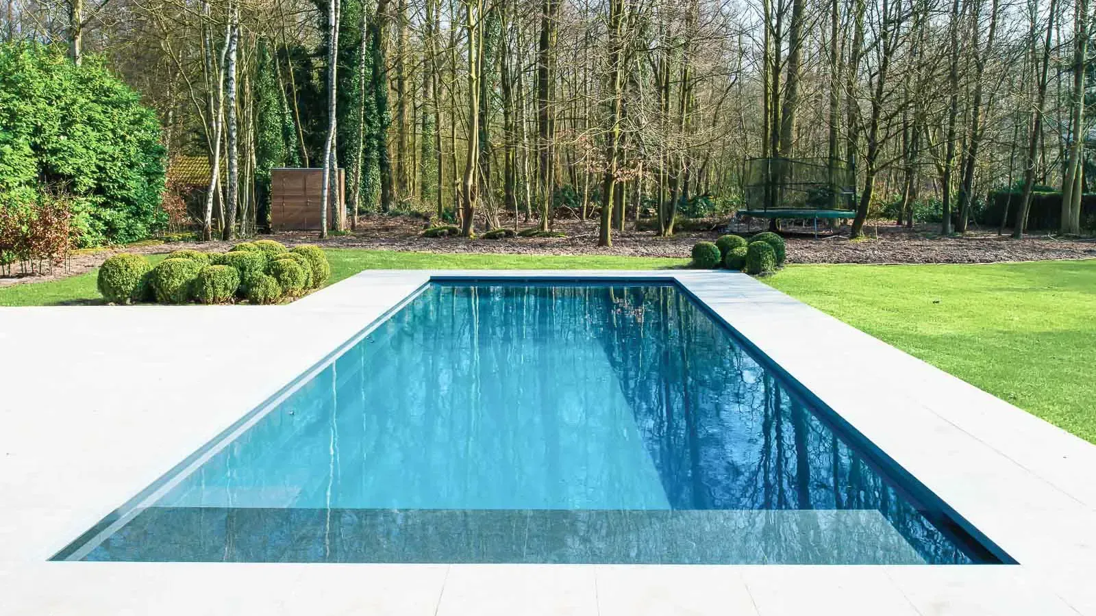 Rectangular outdoor swimming pool with clear blue water, surrounded by a white deck and trees
