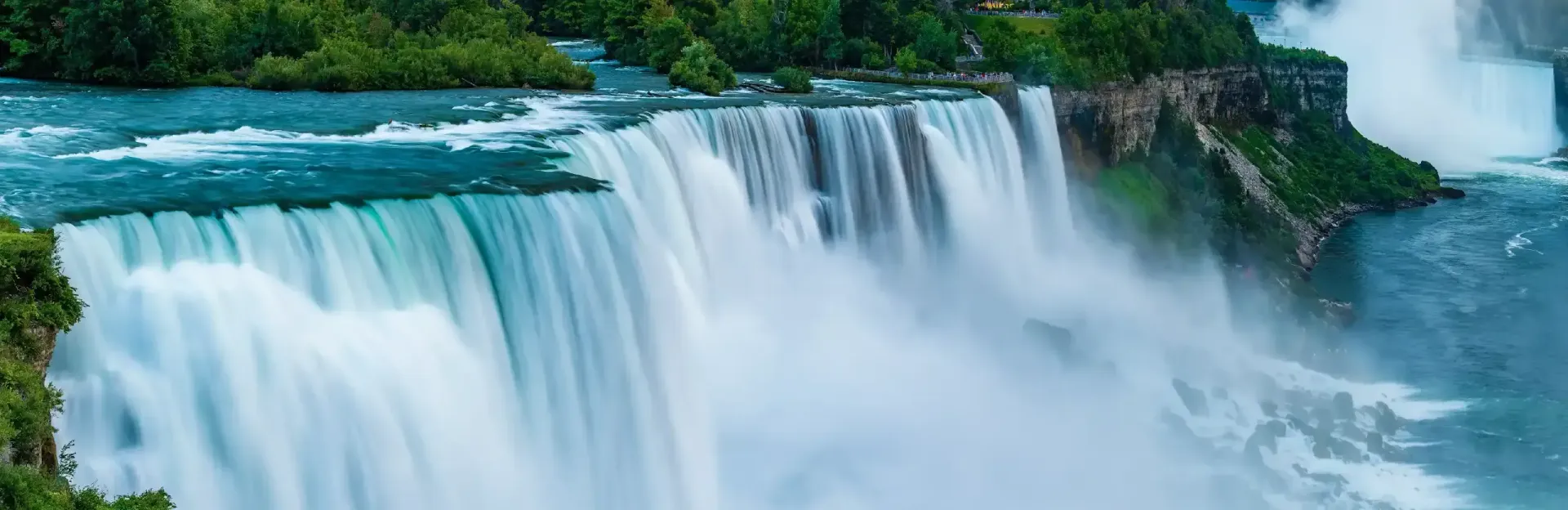 Wide waterfall spilling over a rocky cliff amid lush green forest and mist