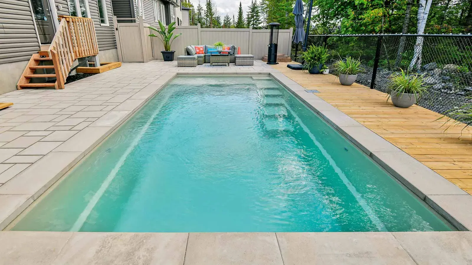 Backyard swimming pool with turquoise water, stone patio, lounge chairs, and a wooden deck