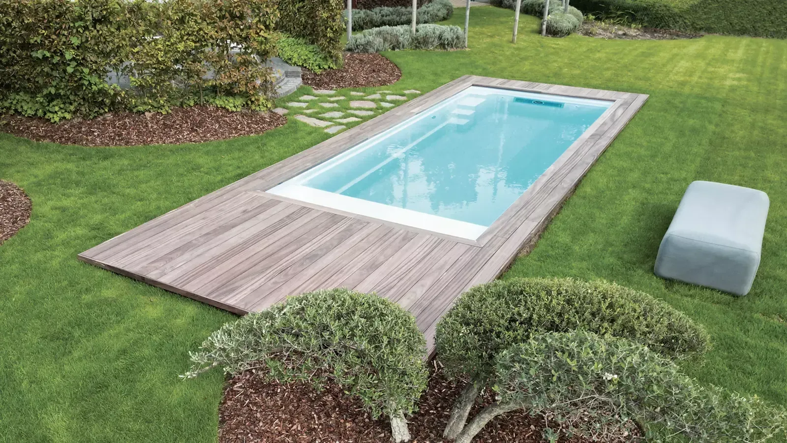 Rectangular backyard pool with clear blue water, surrounded by wood decking and green grass.