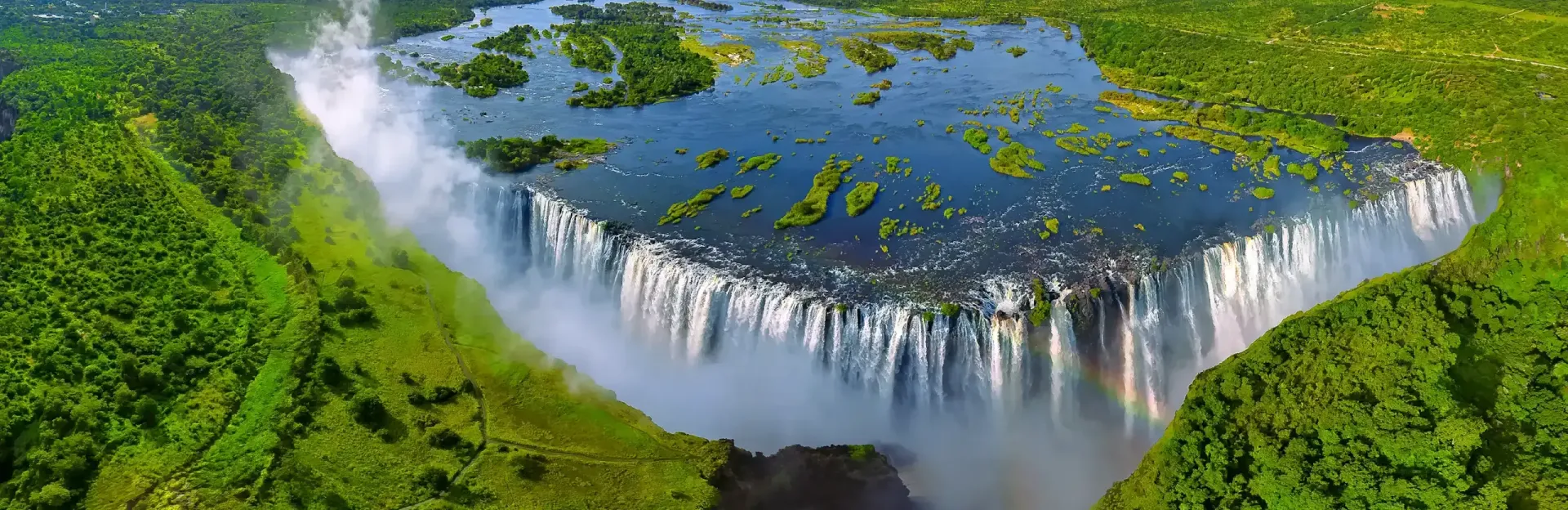 Aerial view of a wide waterfall pouring over a lush green cliff into a river below