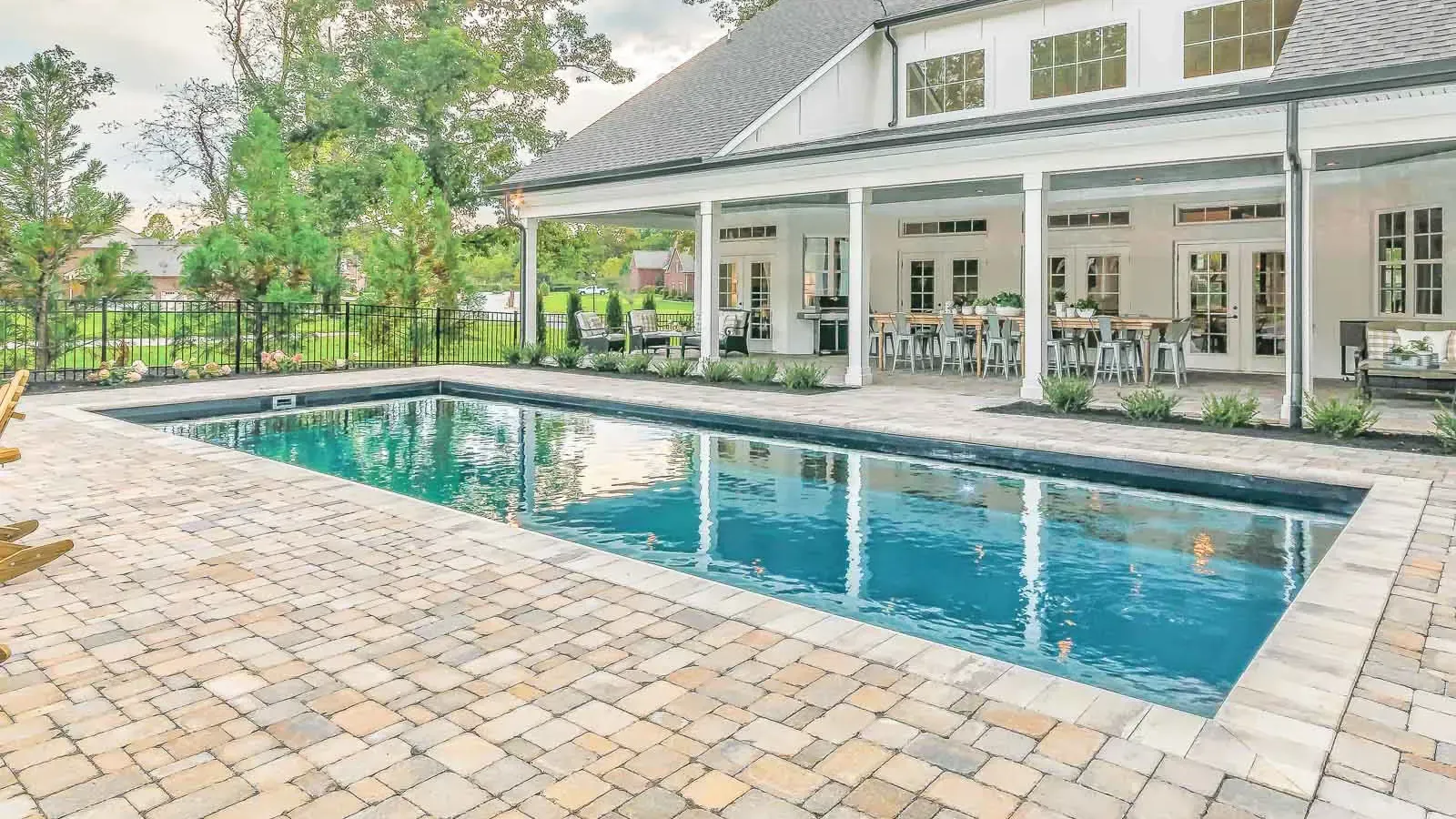 Backyard pool beside a covered patio with white columns and a brick paver deck