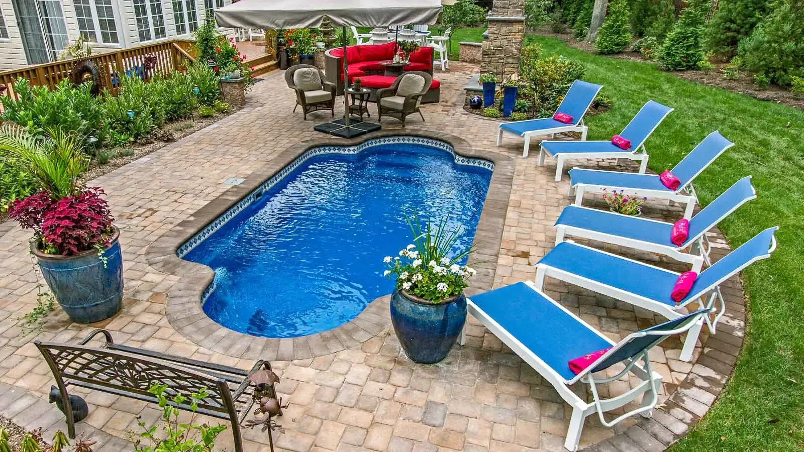 Backyard patio with a small blue pool, lounge chairs, potted flowers, and red seating area