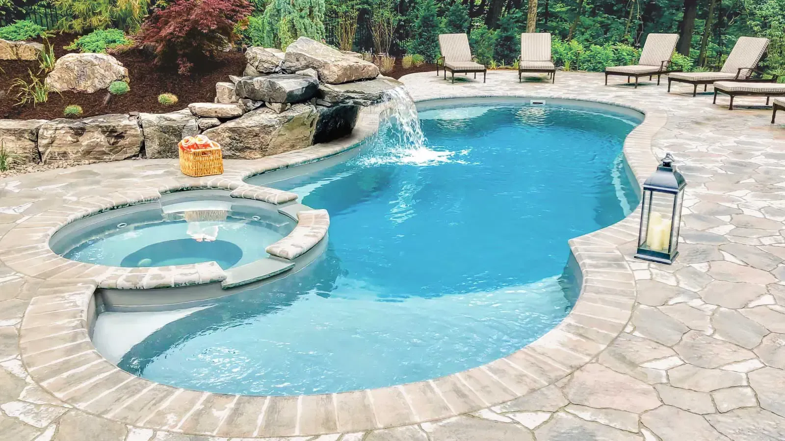 Curved backyard pool with spa, stone patio, lounge chairs, and garden waterfall feature