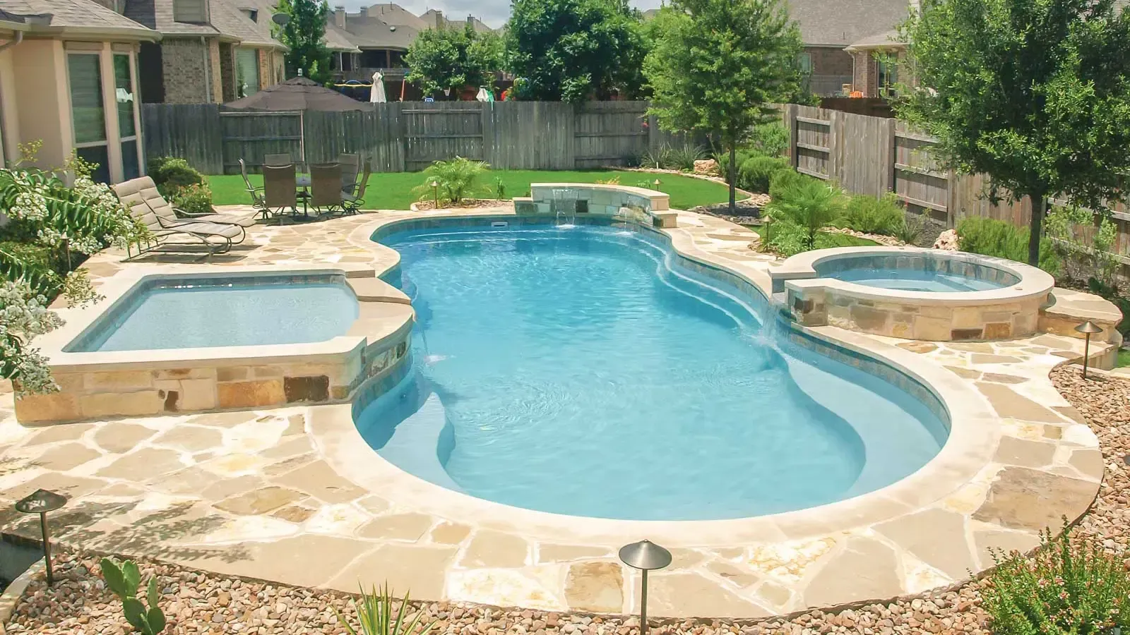 Backyard swimming pool with a spa and stone patio in a residential courtyard