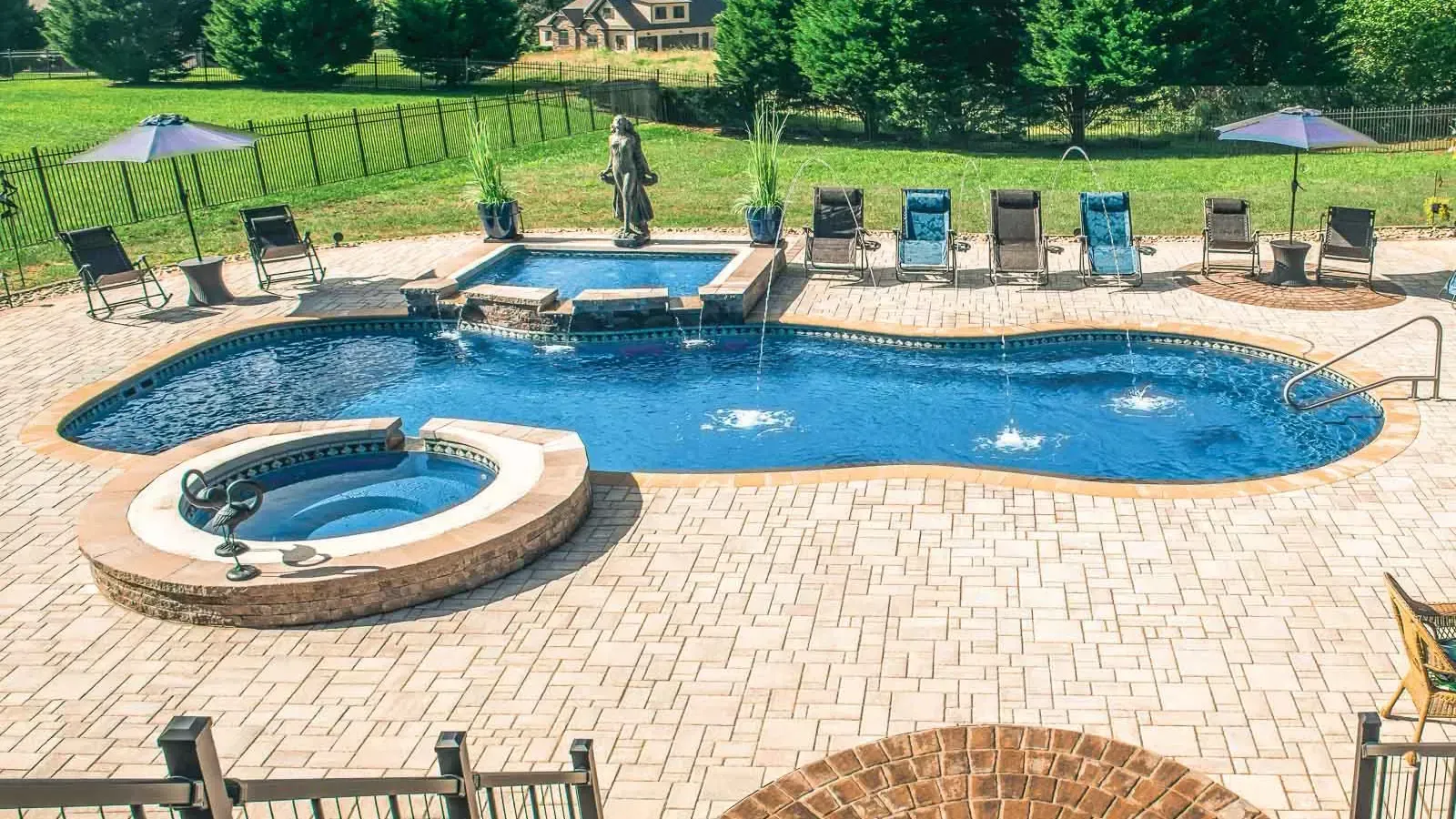 Backyard pool with a circular spa, lounge chairs, and a person standing near the water.