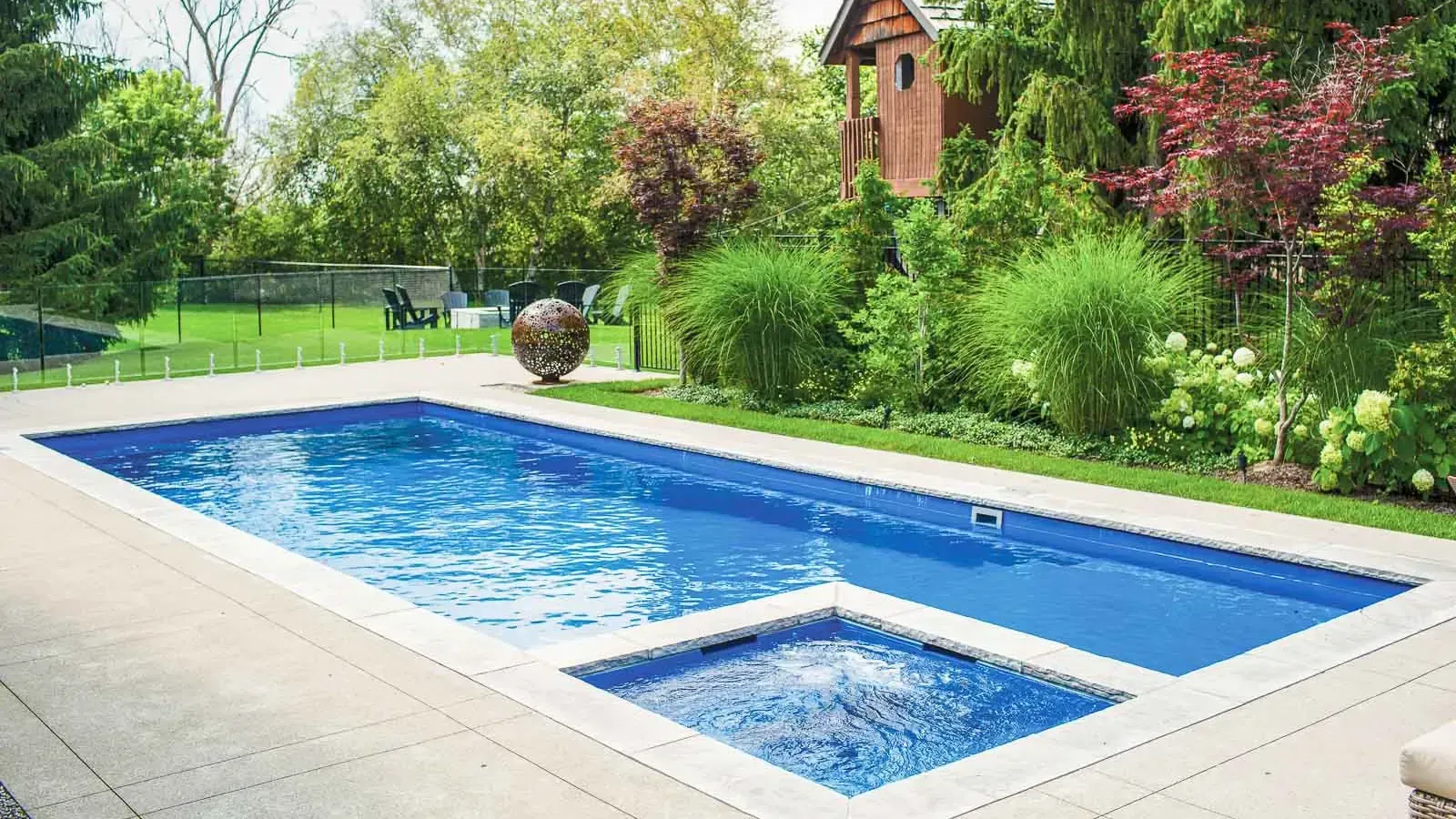Backyard swimming pool with blue water, surrounded by lush green garden and patio tiles