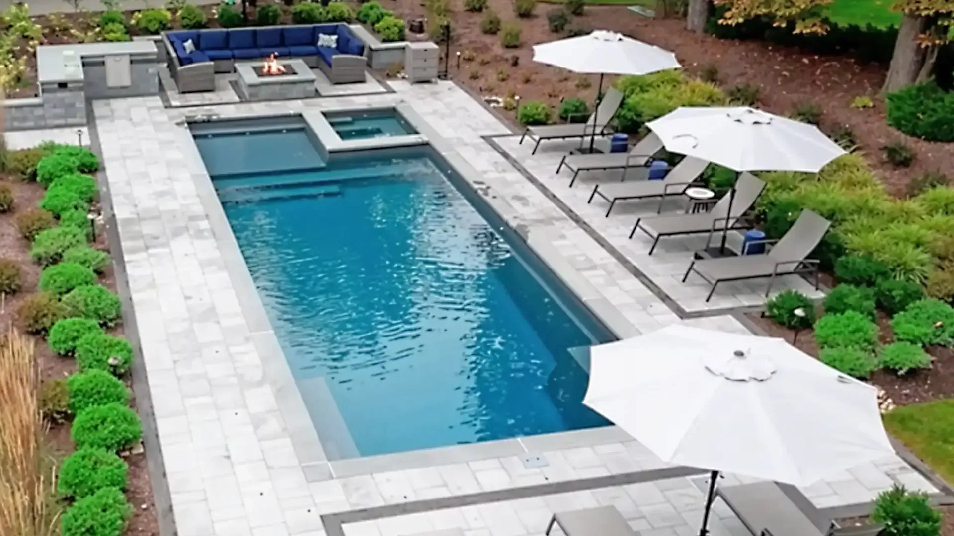 Rectangular backyard pool with lounge chairs, white umbrellas, and a blue cushioned seating area