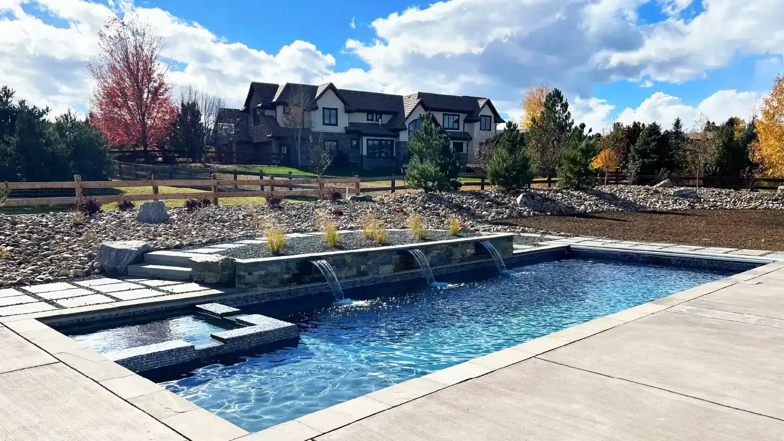 Modern backyard pool with blue water, stone steps, and landscaped seating area under a bright sky