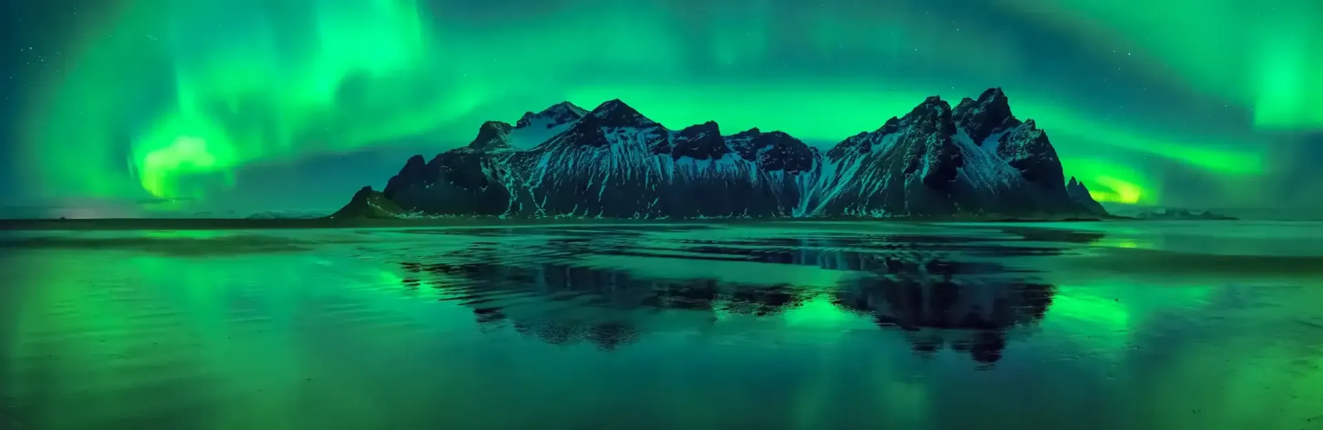 Northern lights glowing green over a snow-covered mountain reflected in still water at night