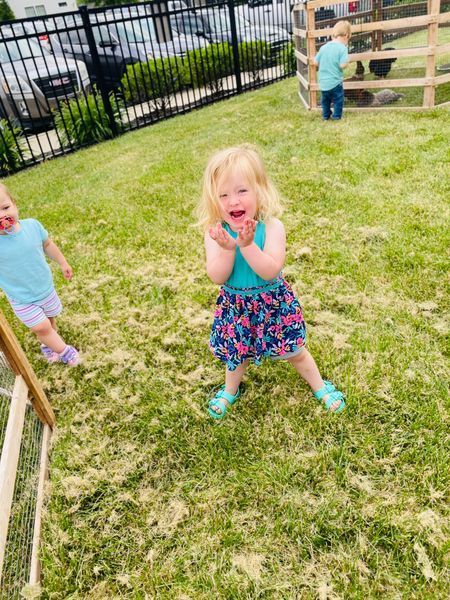 A little girl is standing in the grass in front of a fence.