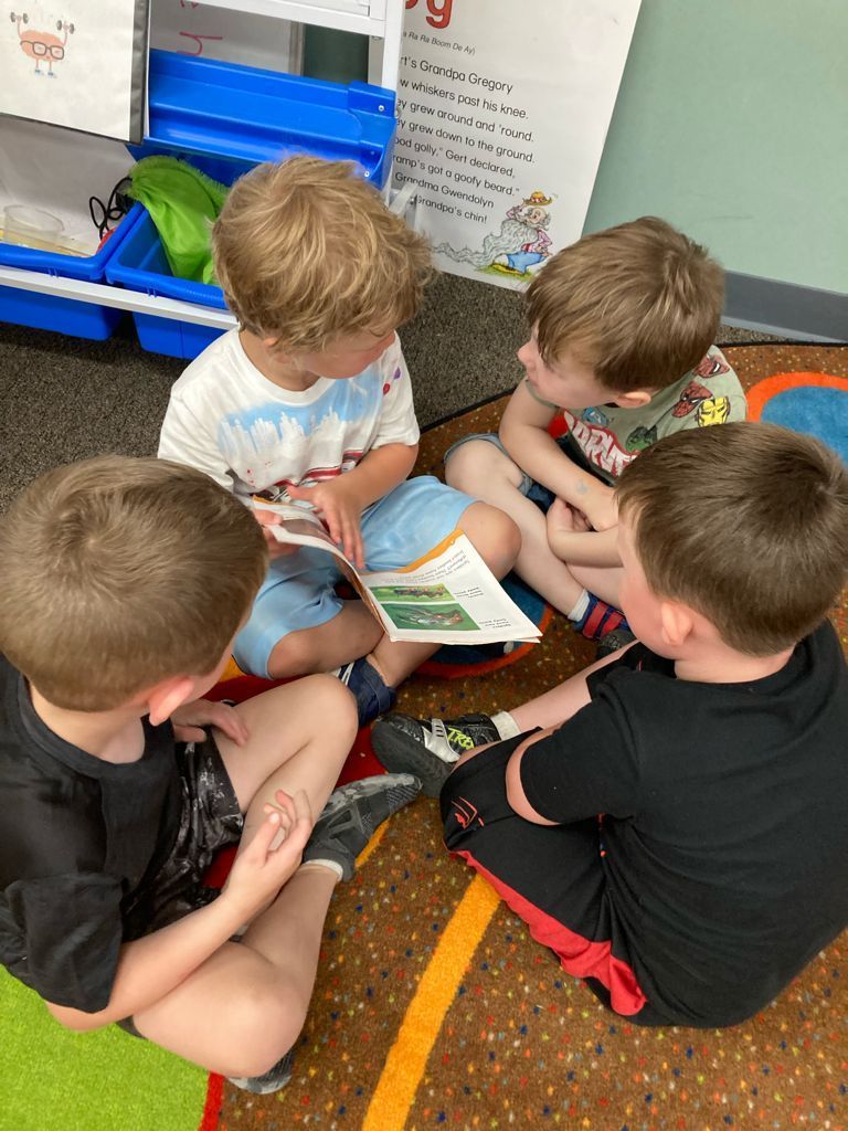 A group of young boys are sitting on the floor reading a book.