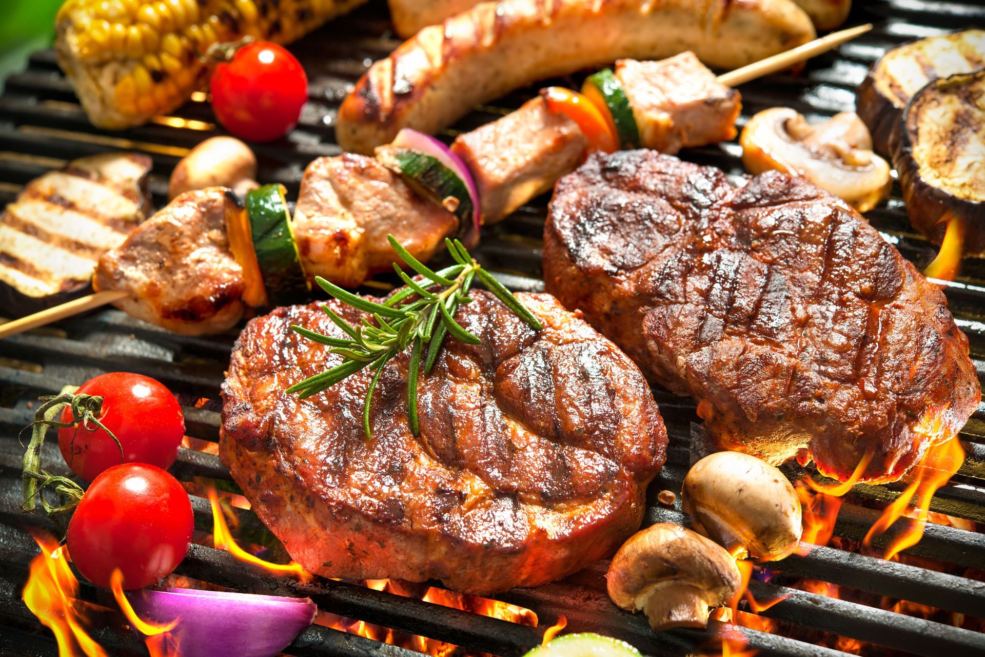 A variety of meats and vegetables are cooking on a grill.