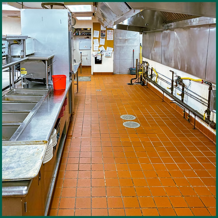 Industrial kitchen with orange tile floor, stainless steel counters, and large ventilation hood