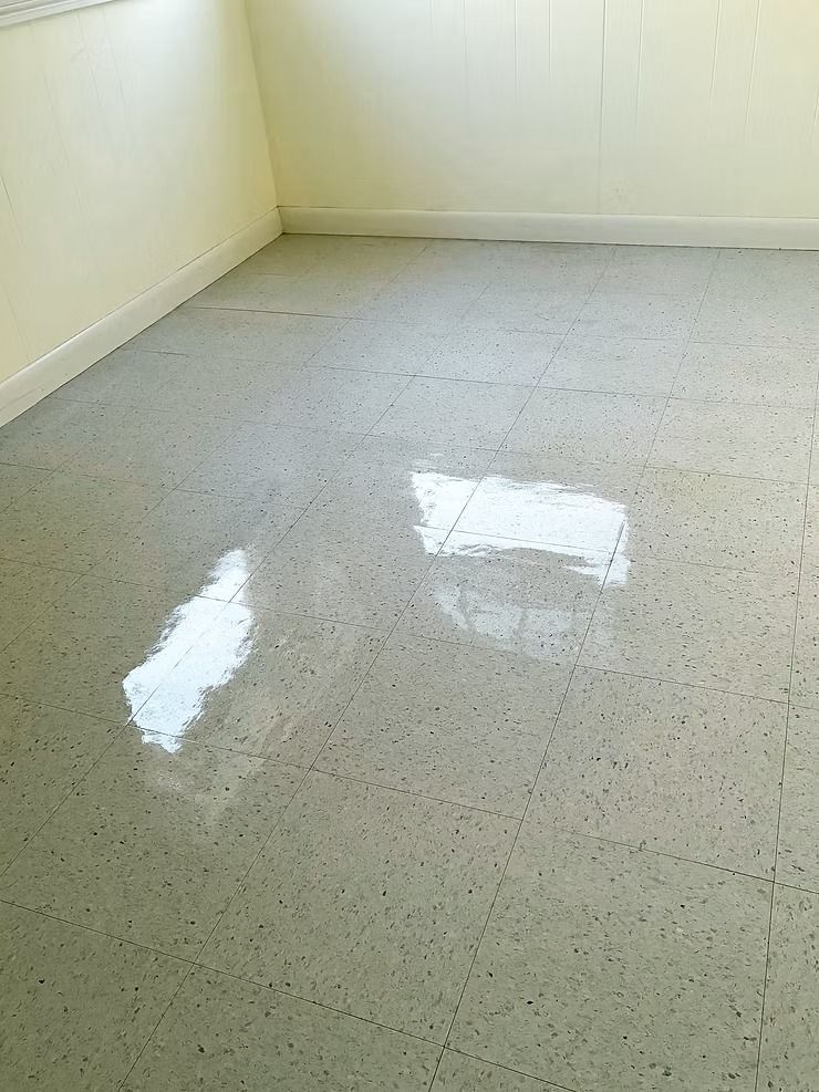 Empty room with light-colored walls and a glossy speckled floor reflecting a window