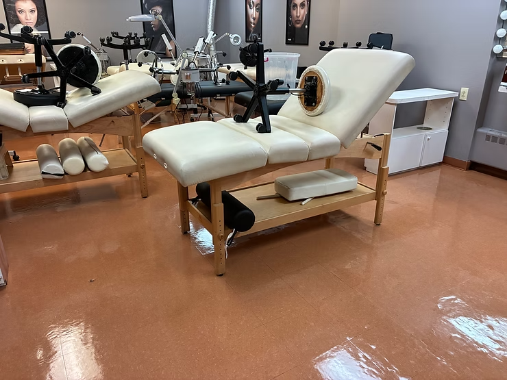 Salon treatment bed with white cushions and a tan wood frame in a mirrored room.