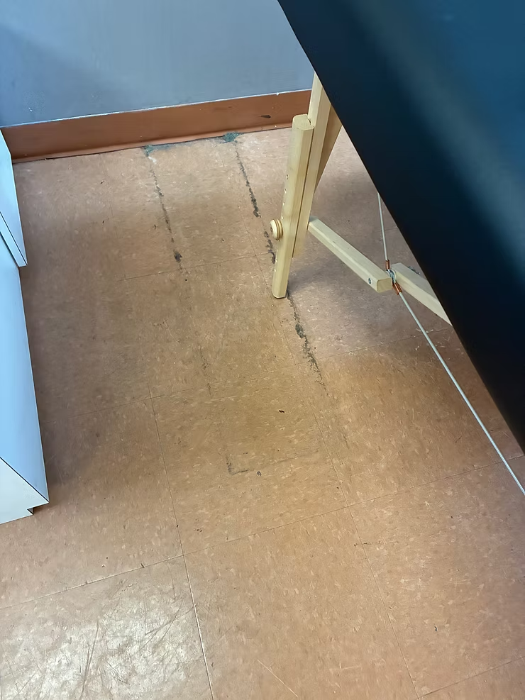 Floor corner with tan linoleum, blue wall, and a wooden chair leg.