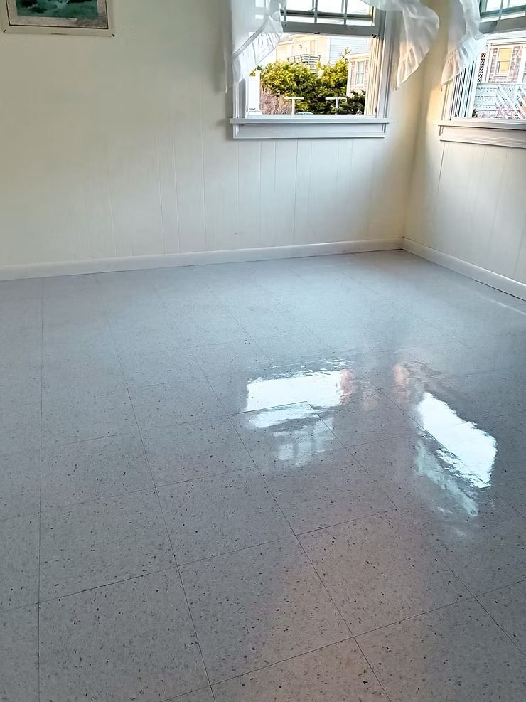 Empty white room with a glossy speckled floor and a window letting in daylight.