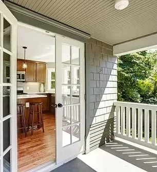 Covered porch with white railings and open French doors to a wood-floored kitchen.
