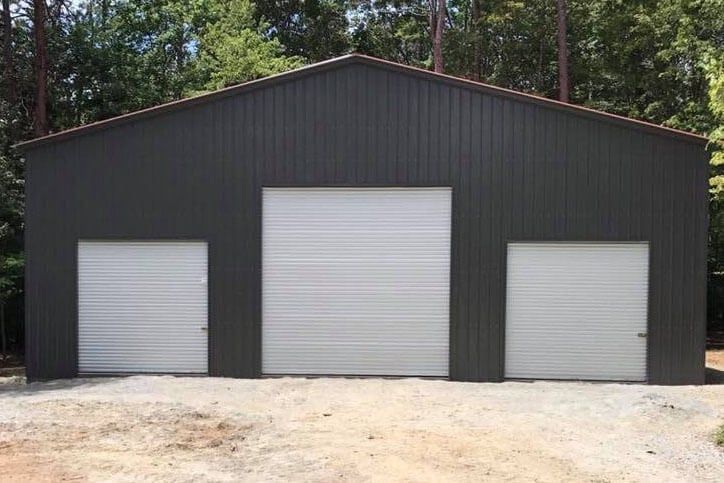 A black metal garage with three white garage doors.