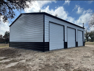 A white and black garage with three garage doors is sitting in the middle of a dirt field.