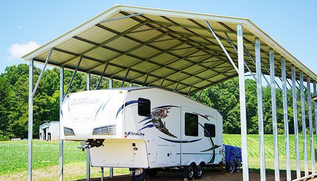 a white RV is parked under a canopy in a field